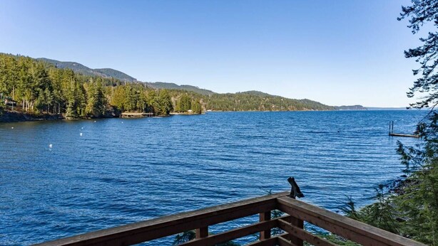A wooden deck overlooking a calm lake with swans, surrounded by dense forest and distant hills. - Stunning views, Strong Wi-fi, and Private Beach! (Lilliwaup)