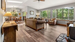 A spacious living room with a large window, a ceiling fan, and a dining area with a table and chairs. - Stunning views, Strong Wi-fi, and Private Beach! (Lilliwaup)