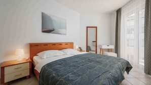 A hotel room with a bed, a nightstand, a desk, a mirror, and a window with curtains. - Holiday apartment with air conditioning, internet and private parking space (Savudrija)