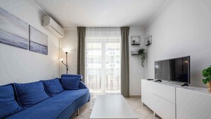 A modern living room with a blue sofa, a white coffee table, a TV on a white cabinet, and a large window with curtains. - Holiday apartment with air conditioning, internet and private parking space (Savudrija)