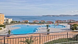 A swimming pool with a curved design, surrounded by buildings with red-tiled roofs, and a view of the sea in the background. - Holiday apartment with air conditioning, internet and private parking space (Savudrija)