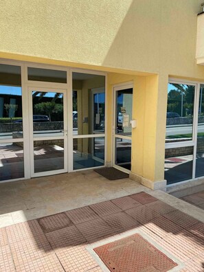 Une entrée d’immeuble avec des portes en verre et un mur extérieur jaune.