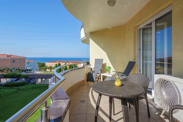 A balcony with a view of the sea, a table with chairs, and a potted plant.