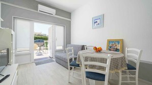 A modern living room with a dining area, a sofa, a TV, and a table with chairs. - Holiday apartment for 2 people on the ground floor (Umag)