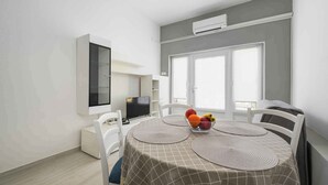 A dining area with a table set for two, a fruit bowl, and a television on a stand. - Holiday apartment for 2 people on the ground floor (Umag)