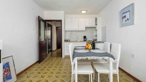 A compact kitchen with white cabinets, a dining table with chairs, and a patterned floor. - Holiday apartment for 2 people on the ground floor (Umag)