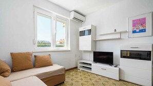 A modern living room with a sofa, TV, and air conditioning unit. - Holiday apartment for 2 people on the ground floor (Umag)