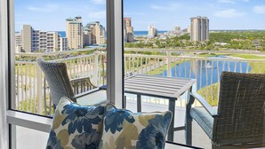 Varanda com cadeiras de vime e uma mesa, com vista para um horizonte urbano e um corpo de água.