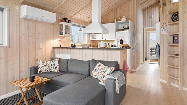 A cozy cabin interior with a grey sofa, wooden walls, a kitchen area, and a small dining table. - Cozy home in Vordingborg with WiFi (Vordingborg)