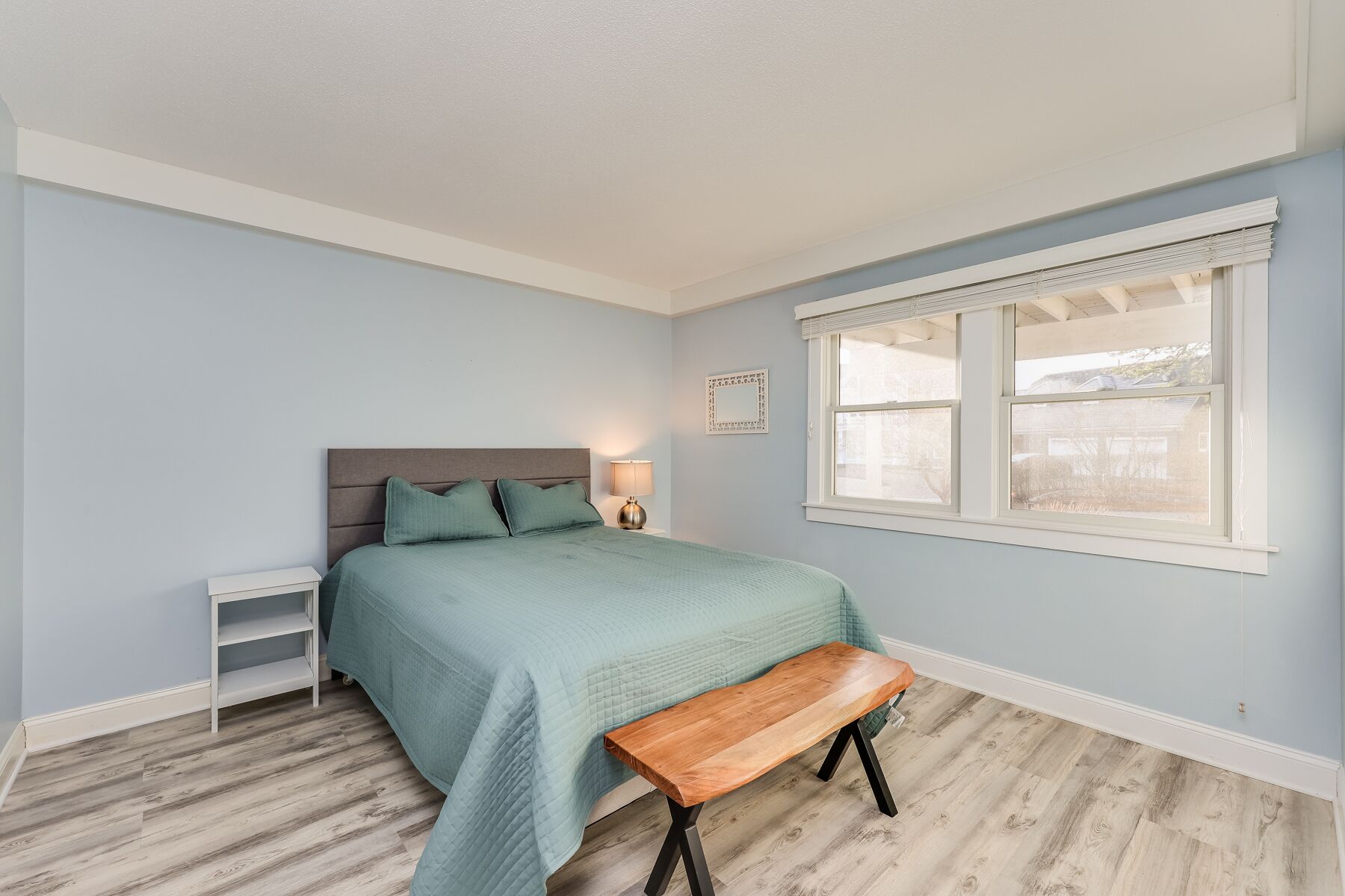 A bedroom with a bed, bedside table, bench, and window.