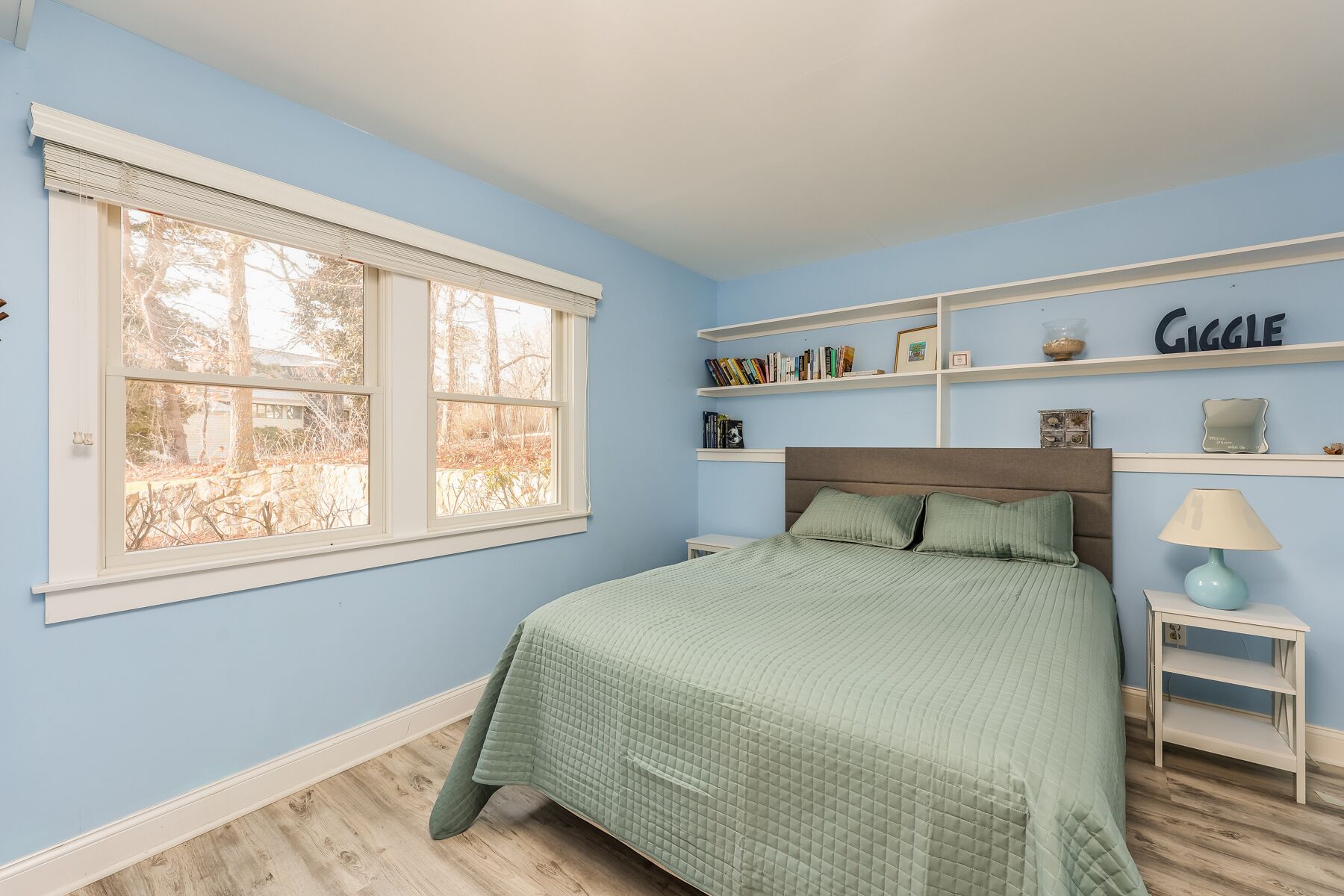 Une chambre à coucher avec un lit, une fenêtre et des étagères remplies de livres et d’objets décoratifs.