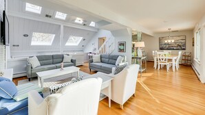 Un vaste salon doté d’un haut plafond, de fenêtres de toit et d’un coin repas avec des meubles blancs.