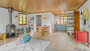 Un vaste salon doté d’un plafond en bois, d’une cheminée, d’un coin repas et d’une cuisine avec des meubles bleus.