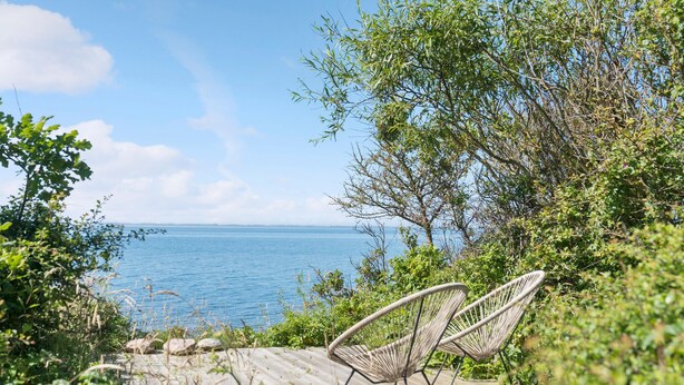 Une terrasse en bois avec deux fauteuils en osier donnant sur une mer calme.