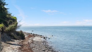Un paysage côtier avec une rive rocheuse, un ciel dégagé et un navire visible à l’horizon.