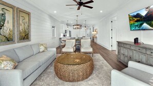 A spacious living room with a large round woven coffee table, a gray sofa, and a television mounted on the wall.