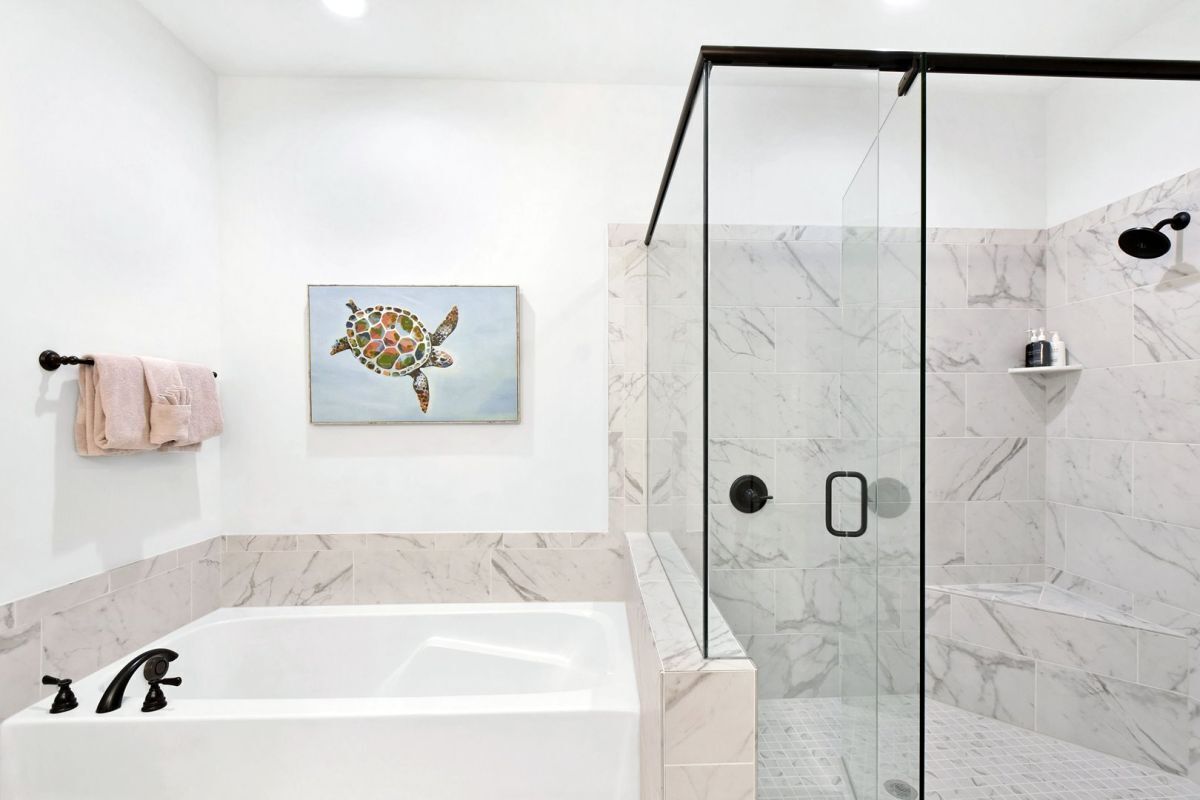 A modern bathroom with a glass-enclosed shower, a marble-tiled wall, and a bathtub.