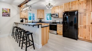 A modern kitchen with wooden cabinets, a black refrigerator, stainless steel appliances, and a bar area with stools. - Make the Family Memories Here | Fishing Pond | Indoor Playground | Scenic Views (Nashville)