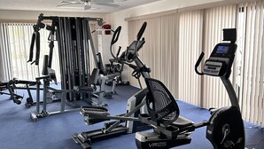 Een fitnessruimte met cardioapparaten, gewichten en een plafondventilator.