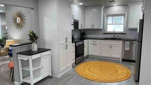 A modern kitchen with white cabinets, a black countertop, and a yellow rug. - Hot Tub- Rose District-Walk to Shopping & Dining (Broken Arrow)