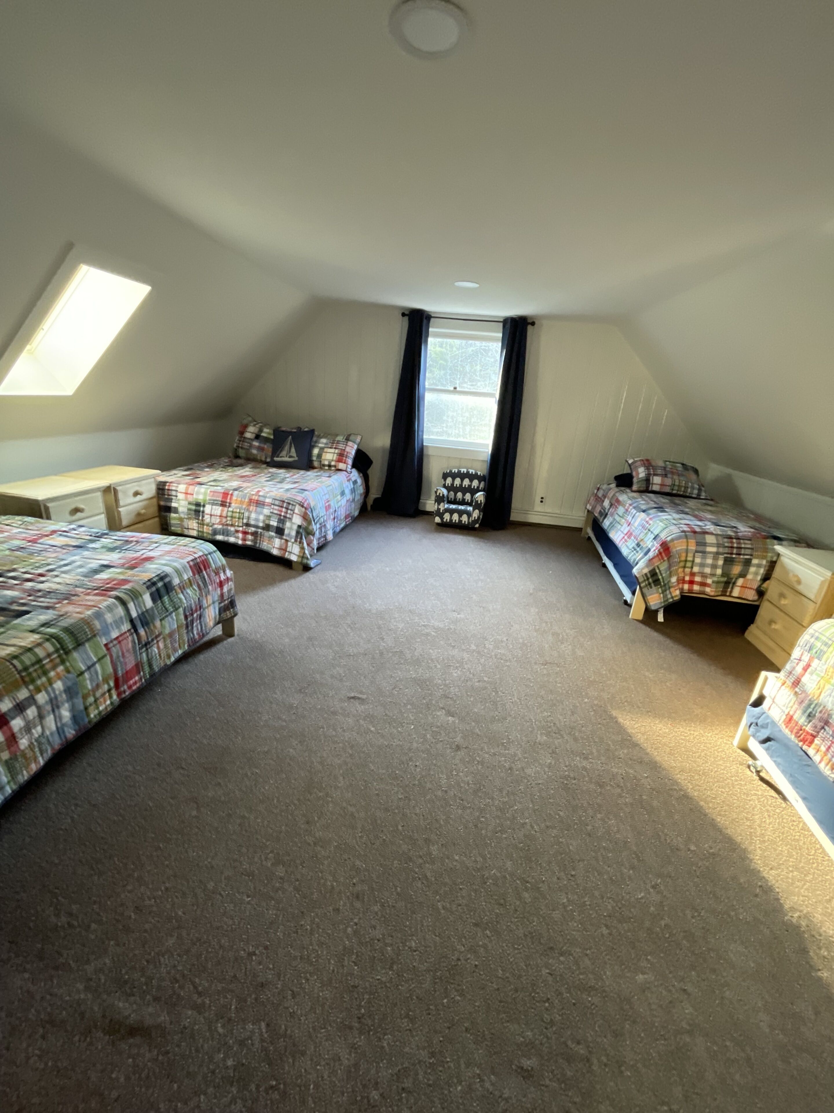A room with three beds, a skylight, and a window with curtains.