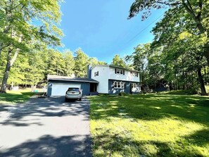 Une maison à deux étages avec un garage, entourée d’arbres et d’une pelouse bien entretenue.