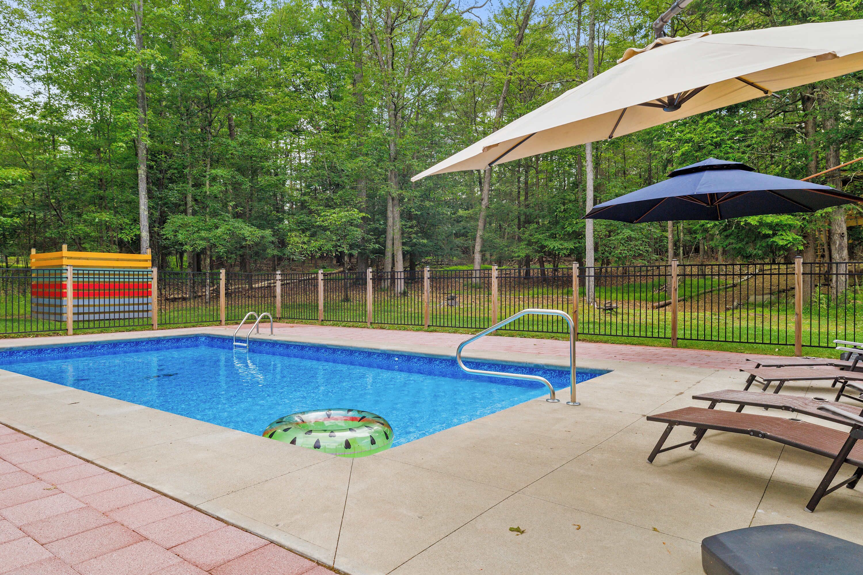 A swimming pool with a ladder, lounge chairs, and umbrellas.