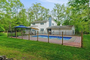 Une maison avec un jardin clôturé, une piscine et un patio couvert.