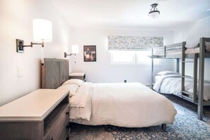 Une chambre avec un lit simple, une table de chevet, une commode, un lit superposé et une fenêtre donnant sur un beau paysage.