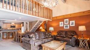 A spacious living area with a high ceiling, wooden staircase, and a kitchen in the background. - Snowcreek #309  2 Plus Loft, 2 Bathroom Condo Sleeps 8 People with Amazing Mountain Views (Mammoth Lakes)