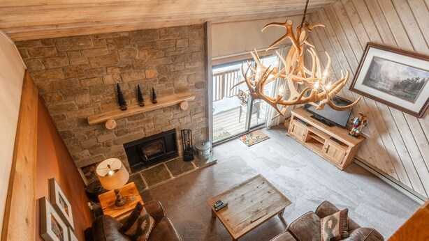 A cozy living room with a stone fireplace, leather sofa, wooden coffee table, and a chandelier. - Snowcreek #309  2 Plus Loft, 2 Bathroom Condo Sleeps 8 People with Amazing Mountain Views (Mammoth Lakes)