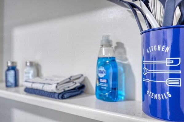 A kitchen utensil holder with utensils and cleaning supplies on a white shelf.