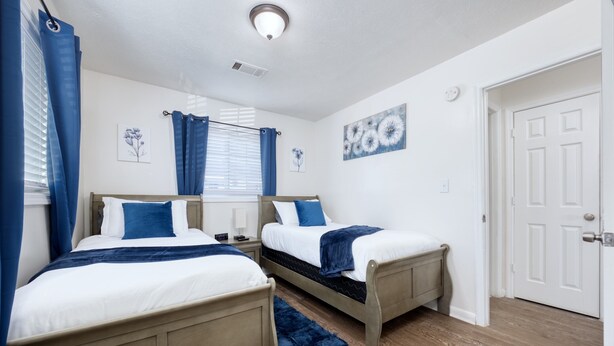 A bedroom with two beds, a blue rug, and a white door.