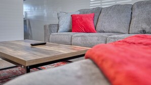 A modern living room with a grey sofa, a wooden coffee table, and a red throw blanket.