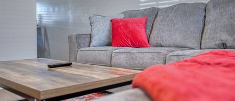 Una sala de estar moderna con un sofá gris, una mesa de centro de madera y una manta roja.