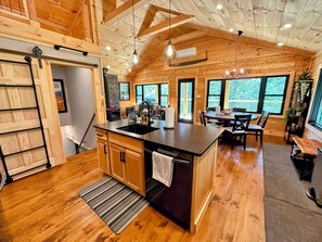 A spacious kitchen with wooden cabinets, a large island, and a dining area with a table and chairs. - 5R Cozy log chalet in fantastic location. Ski, snowshoe, fish, explore! AC, and dog friendly! (Bethlehem)