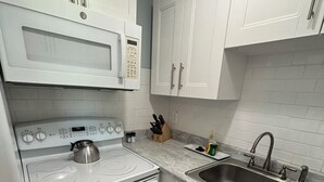 Een moderne keuken met witte kasten, een roestvrijstalen spoelbak, een ingebouwde magnetron en een gasfornuis.