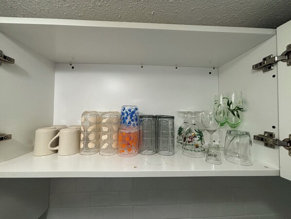 Une étagère blanche sur laquelle sont disposés divers objets en verre, notamment des verres, une carafe et des verres à vin.