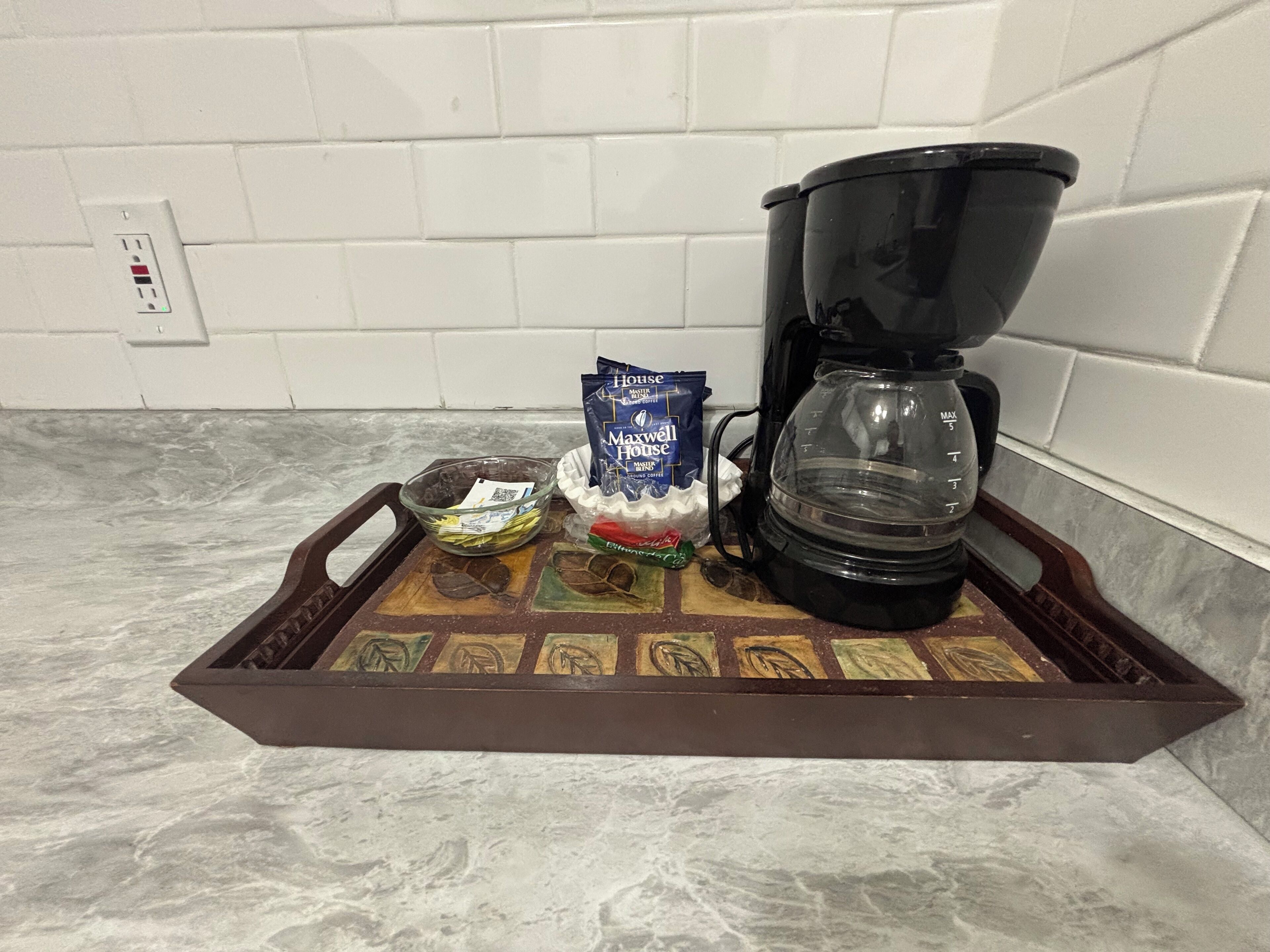 Un plateau contenant une cafetière, un paquet de café Maxwell House, un bol avec une cuillère et un petit sachet de sucre.