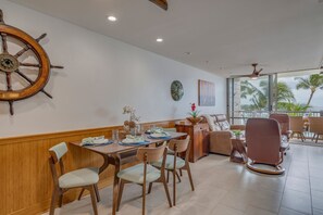 Un espace repas avec des meubles en bois, une roue de navire et une vue sur les palmiers à travers de grandes fenêtres.