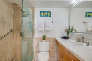 Une salle de bain moderne avec une douche à parois de verre, des toilettes blanches, un lavabo avec un plan de toilette en marbre et des serviettes décoratives.