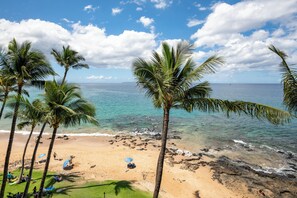A beach with palm trees, clear blue water, and a sandy shore.