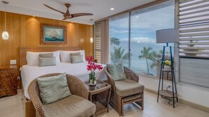 A spacious bedroom with a large bed, two wicker chairs, a nightstand, and a view of the ocean through large windows. - Stunning retreat with oceanfront views (Kihei)