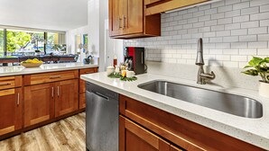 Una cocina moderna con armarios de madera, un lavamanos de acero inoxidable y un salpicadero de azulejos blancos.