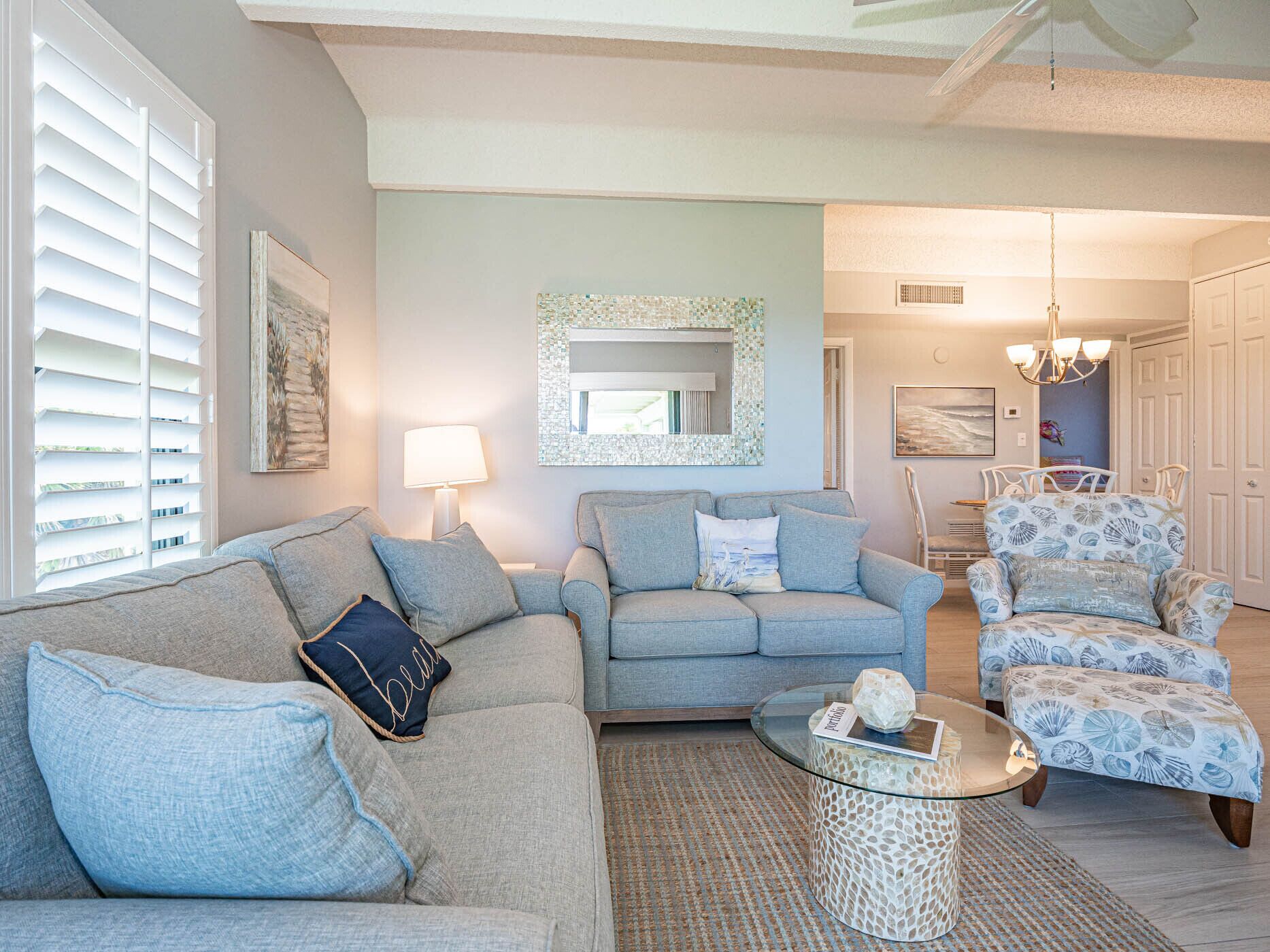 A living room with a light blue sofa, a patterned armchair, and a glass coffee table.