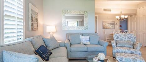 A living room with a light blue sofa, a patterned armchair, and a glass coffee table.