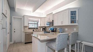 A kitchen with white cabinets, a central island with bar stools, and a microwave. - Ocean front condo,  walk to quaint Vero Beach restaurants and shops.  (Vero Beach)