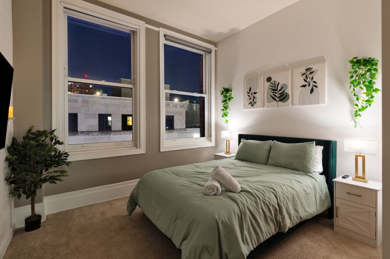 A bedroom with a bed, nightstands, a potted plant, and artwork on the wall.