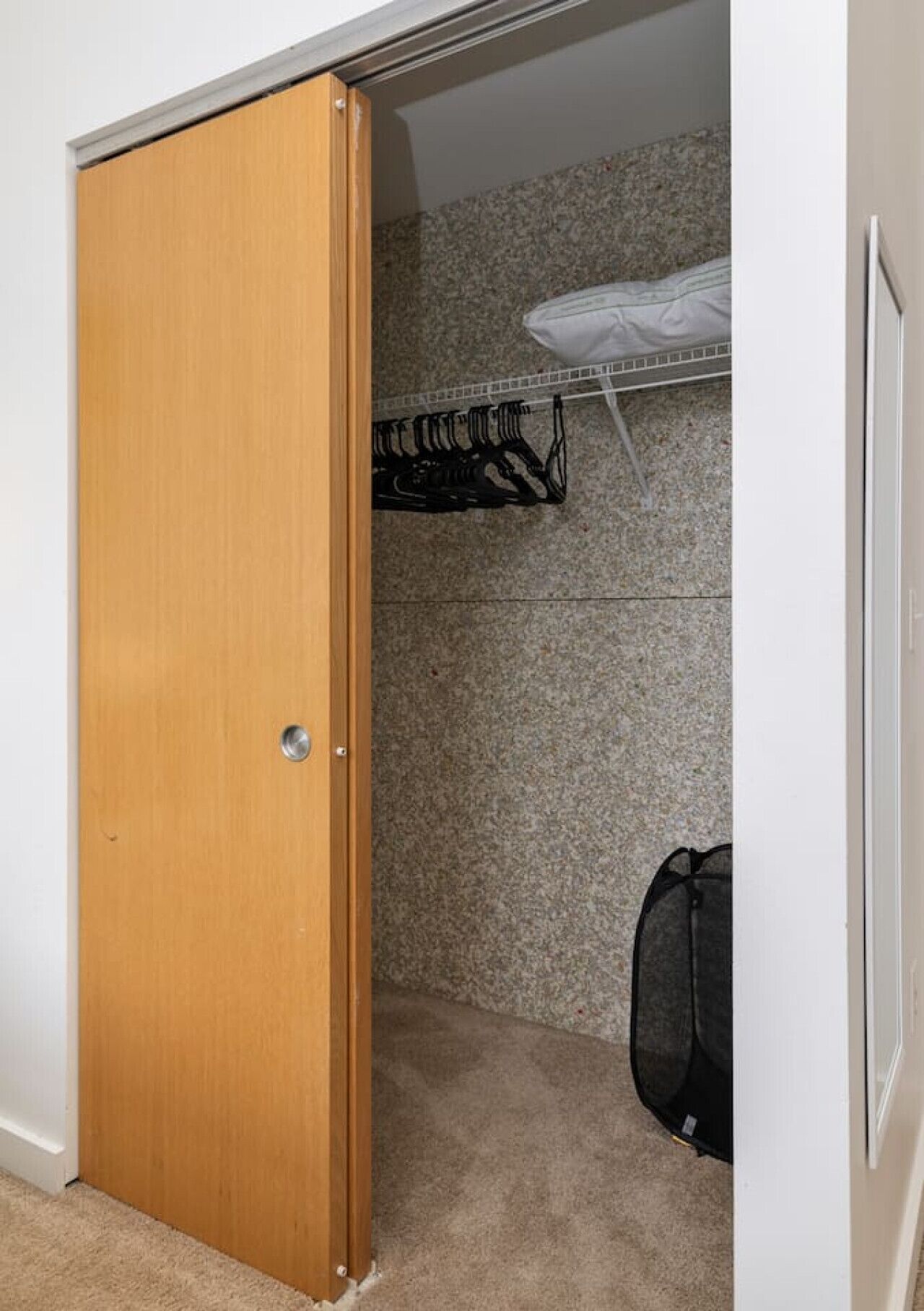Un placard avec une porte en bois, une tringle à vêtements et un sac à dos posé sur le sol.