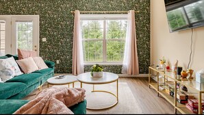 A living room with a green sofa, a round coffee table, and a TV mounted on the wall. - A thoughtfully designed 3-bedroom, 2.5-bath townhome tailored for travelers. (Chambersburg)